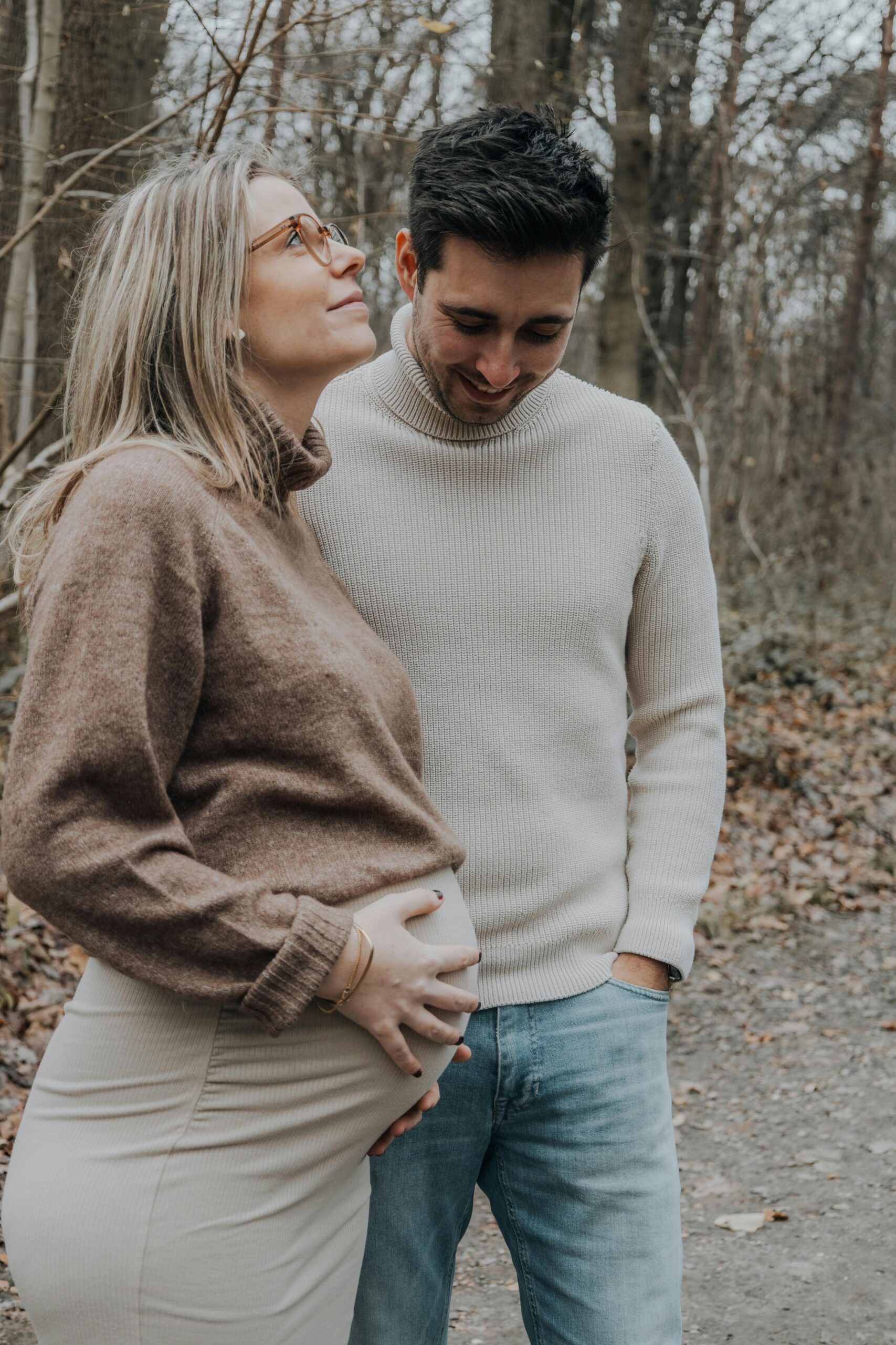 A happy pregnant couple embracing and smiling during a walk in an autumn forest.