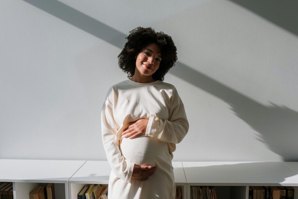 Expert <br>Ouders van Nu Beautiful pregnant woman with curly hair embracing maternity in a serene indoor setting.